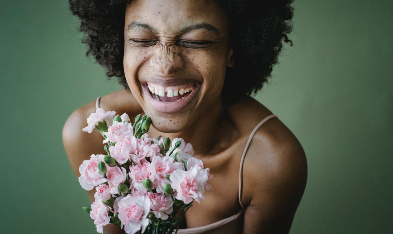 a portrait of a beautiful, happy, woman displaying a peony bouquet of flowers and her bright beautiful smile with her eyes close.