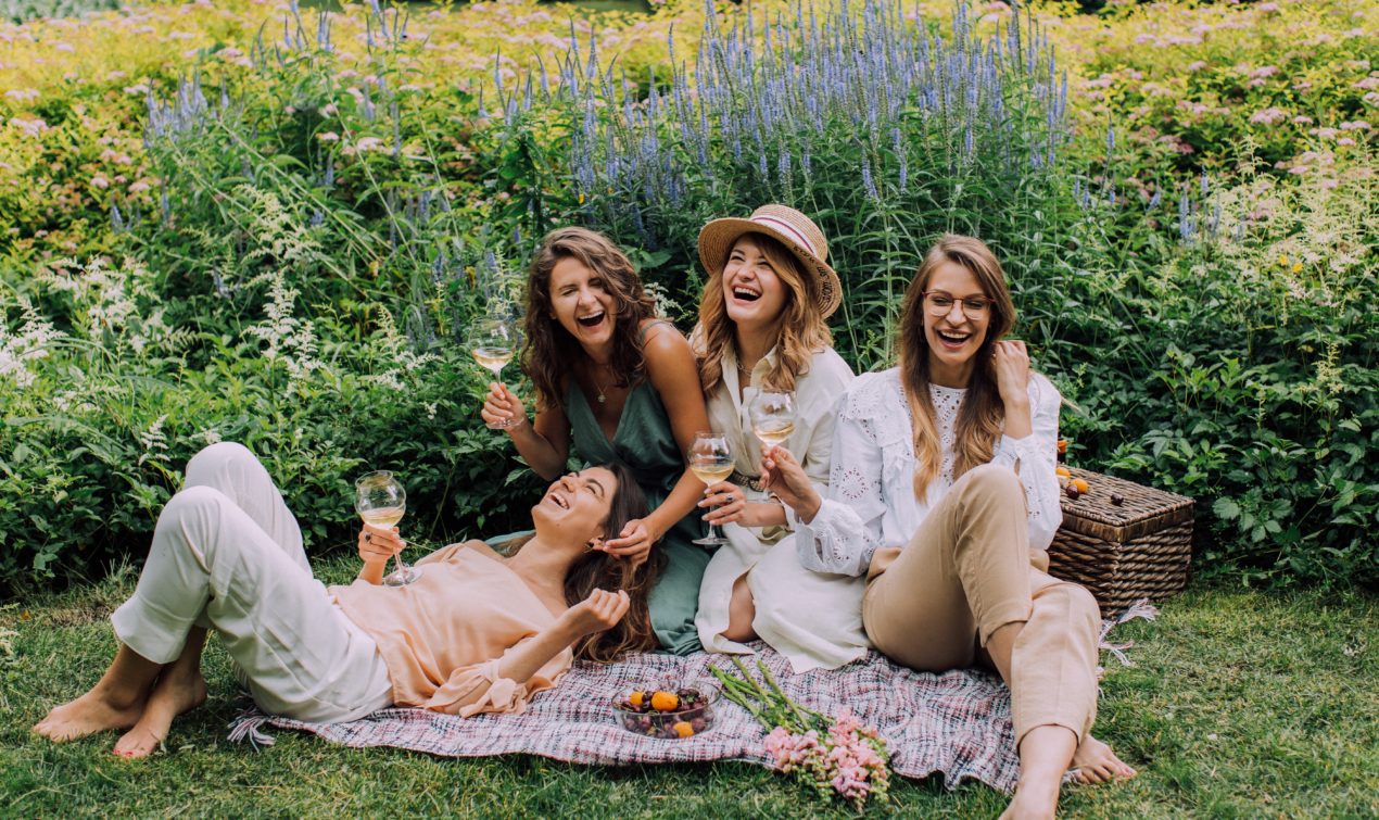 Girlfriends enjoy a picnic and having a good time, laughing and drinking wine.